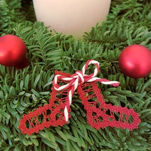 May include: Red bobbin lace Christmas ornaments with a white and red ribbon bow, on a green pine wreath with red ornaments and a white candle.