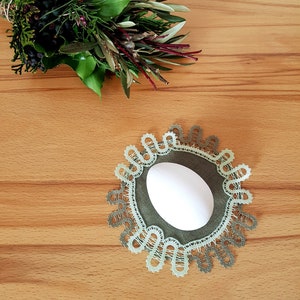 May include: A green bobbin lace doily with a white egg in the centre. The doily is on a wooden surface. The text "bobbin lace patterns by TINA KODER" is in the top right corner of the image.