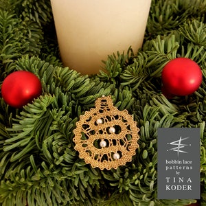 May include: A gold bobbin lace ornament in the shape of a Christmas tree with white beads. The ornament is surrounded by green pine branches and red ornaments. The text "bobbin lace patterns by TINA KODER" is visible in the image.