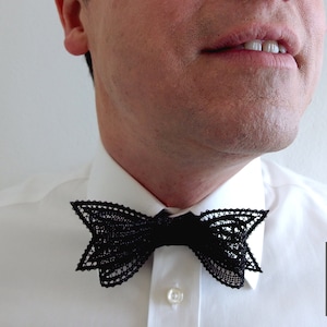 Puede incluir: Una pajarita de encaje negro que lleva una persona con una camisa blanca. La pajarita está hecha con un patrón delicado e intrincado. El texto "bobbin lace patterns by TINA KODER" es visible en la esquina inferior derecha de la imagen.