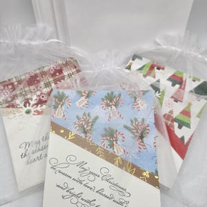 May include: Christmas greeting cards with various festive designs, including candy canes, snowflakes, and Christmas trees. The cards are in clear cellophane bags, with text that reads "May your Christmas be warm with love, blessed with joy, and bright with promise."