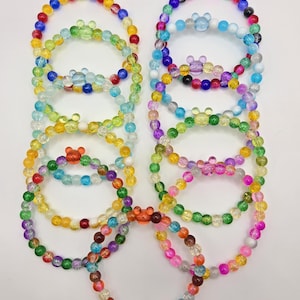 May include: A collection of colorful beaded bracelets. Each bracelet features a variety of colors, including red, blue, green, yellow, and pink. The bracelets are adorned with a small, clear, Mickey Mouse-shaped charm. The beads are small and round, creating a playful and vibrant accessory.