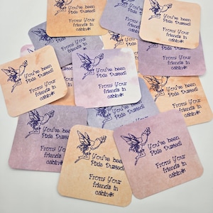 May include: A collection of square, pastel-colored cards with rounded corners. Each card features a purple fairy illustration and the text "You've been Pixie Dusted! From: Your friends in cabin:" in a handwritten style font.