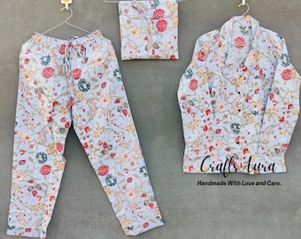 May include: A blue pajama set with a floral print. The set includes a long-sleeved shirt with a button-up front and matching pants. The fabric has a light blue background with red, green, and white floral designs. The text "Crafts Aura Handmade With Love and Care." is printed on the shirt.