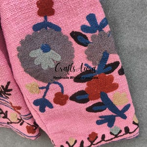 May include: Pink fabric with embroidered floral designs in shades of blue, brown, gray, and beige. The fabric has a textured woven appearance. The text "Crafts Aura Handmade With Love and Care" is visible in the center of the image.