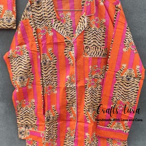 May include: Orange and pink striped pajama top with a tiger print. The top has a button-up front and long sleeves. The text "Crafts Aura Handmade With Love and Care." is printed on the bottom right corner.