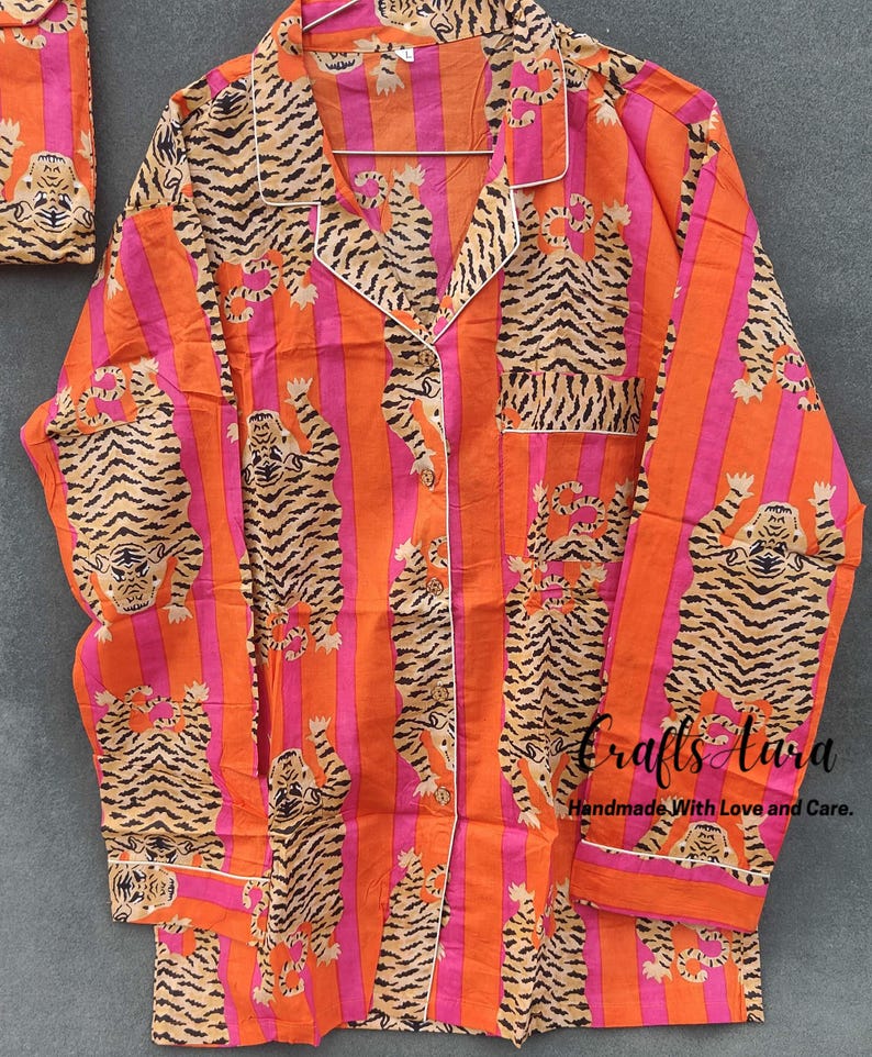 May include: Orange and pink striped pajama top with a tiger print. The top has a button-up front and long sleeves. The text "Crafts Aura Handmade With Love and Care." is printed on the bottom right corner.