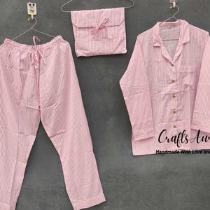 Puede incluir: Conjunto de pijama a rayas rosa con camisa de manga larga y pantalón. La camisa tiene un frente abotonado y un cuello. El conjunto está hecho a mano con amor y cuidado.