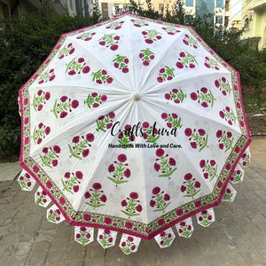 May include: White outdoor umbrella with a floral pattern in red and green. The umbrella has a scalloped edge with matching floral designs. The text "Crafts Aura Handmade With Love and Care" is printed on the umbrella.