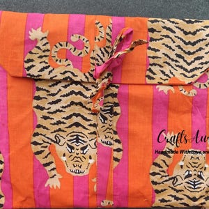 May include: Orange and pink striped fabric with a tiger print. The fabric is folded into a pouch with a pink ribbon tie. The text "Crafts Aura Handmade With Love and Care." is printed on the fabric.