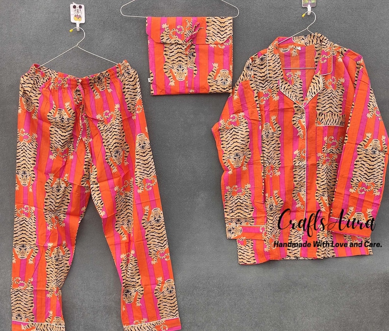 May include: A pajama set with a pink and orange striped pattern featuring a tiger print. The set includes a long-sleeved shirt with a button-up collar and matching pants.