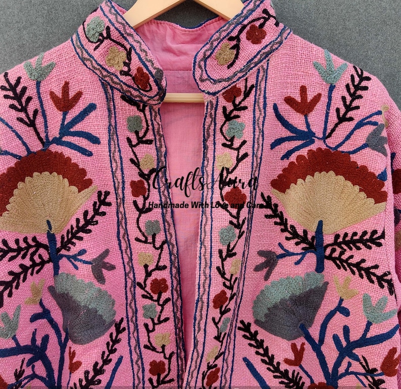 May include: A pink embroidered jacket with a floral design. The jacket has a mandarin collar and a front closure. The embroidery is in shades of brown, blue, and green.