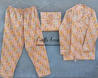 May include: A pajama set with a long-sleeved shirt and pants. The fabric is a light pink and yellow with a floral pattern. The shirt has a collar and a button closure. The pants have an elastic waistband. The text "Crafts Aura Handmade With Love and Care" is visible in the image.