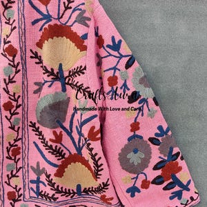 May include: A pink embroidered jacket with a floral pattern in shades of blue, red, brown, and gray. The jacket has a  "Crafts Hub" logo and the text "Handmade With Love and Care".