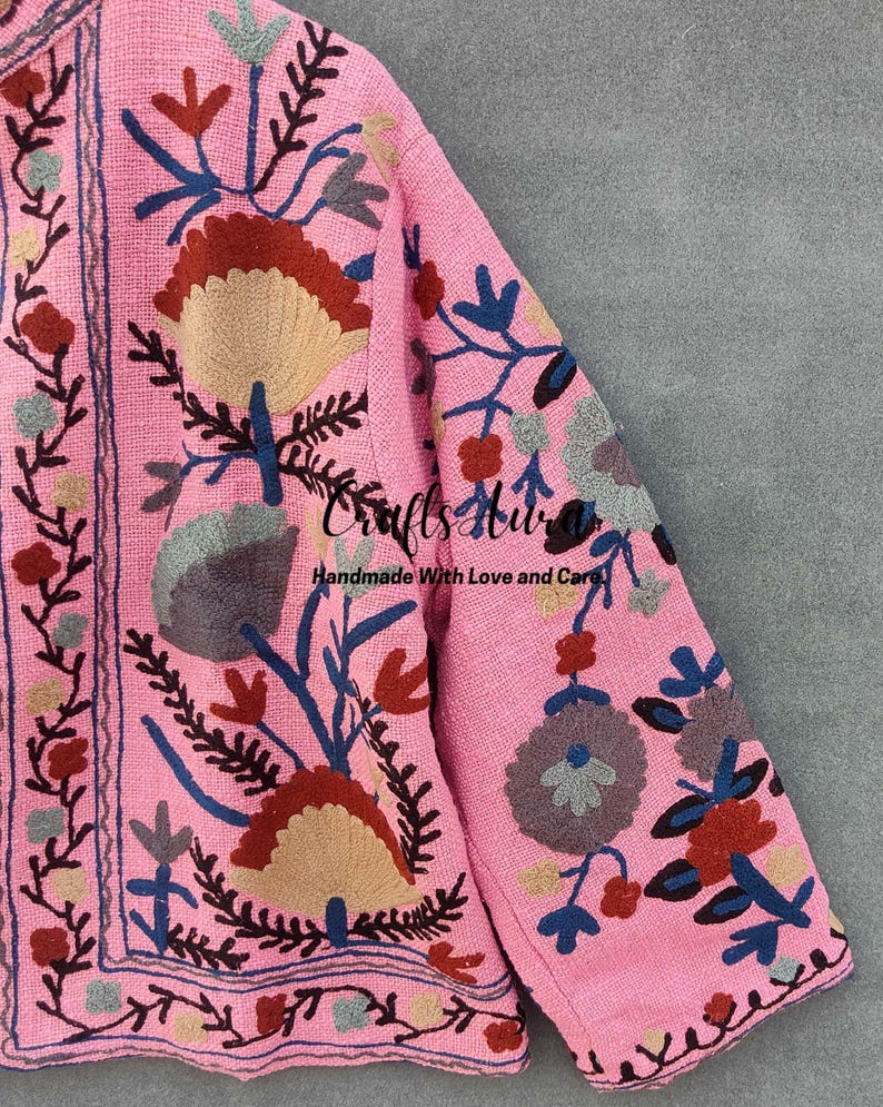 May include: A pink embroidered jacket with a floral pattern in shades of blue, red, brown, and gray. The jacket has a  "Crafts Hub" logo and the text "Handmade With Love and Care".