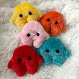 Puede incluir: Cinco peluches con forma de ameba en diferentes colores: amarillo, rosa, naranja, rojo y azul verdoso. Cada peluche tiene dos ojos negros grandes.