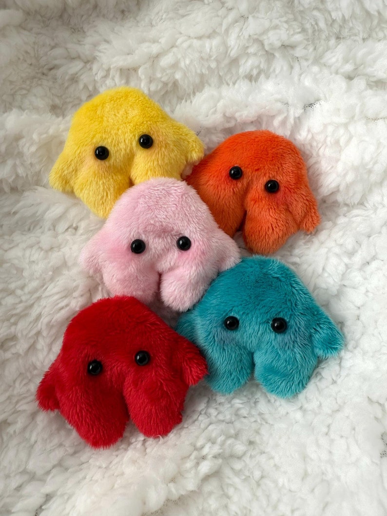 Puede incluir: Cinco peluches con forma de ameba en diferentes colores: amarillo, rosa, naranja, rojo y azul verdoso. Cada peluche tiene dos ojos negros grandes.