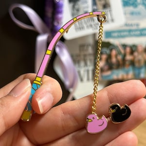 K&ouml;nnte beinhalten: Ein skurriles Emaille-Pin-Set mit einer rosa und gelben Angelrute mit einer goldenen Kette und zwei Enten-Pins. Eine Ente ist rosa, die andere ist schwarz. Die Pins sind wahrscheinlich f&uuml;r eine Jacke, einen Rucksack oder ein anderes Accessoire.