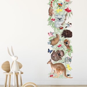 Puede incluir: Una calcomanía de pared colorida con animales australianos, incluyendo un koala, un canguro, un equidna y un ornitorrinco, rodeados de follaje verde y flores.