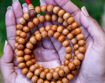 May include: A wooden prayer bead necklace with a red string tassel, held in cupped hands.