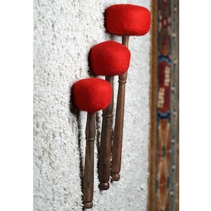 May include: Three wooden mallets with red felt heads, arranged vertically on a white textured wall.