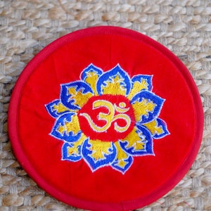 May include: A red circular cushion with an embroidered blue and yellow lotus flower design and the symbol "Om" in the center.
