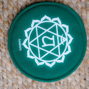 Op de afbeelding: Rond groen kussen met een wit symbool en het woord "Anahata" erop gedrukt.