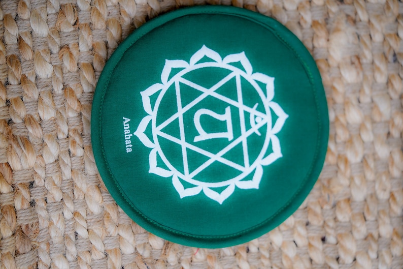 Op de afbeelding: Rond groen kussen met een wit symbool en het woord "Anahata" erop gedrukt.