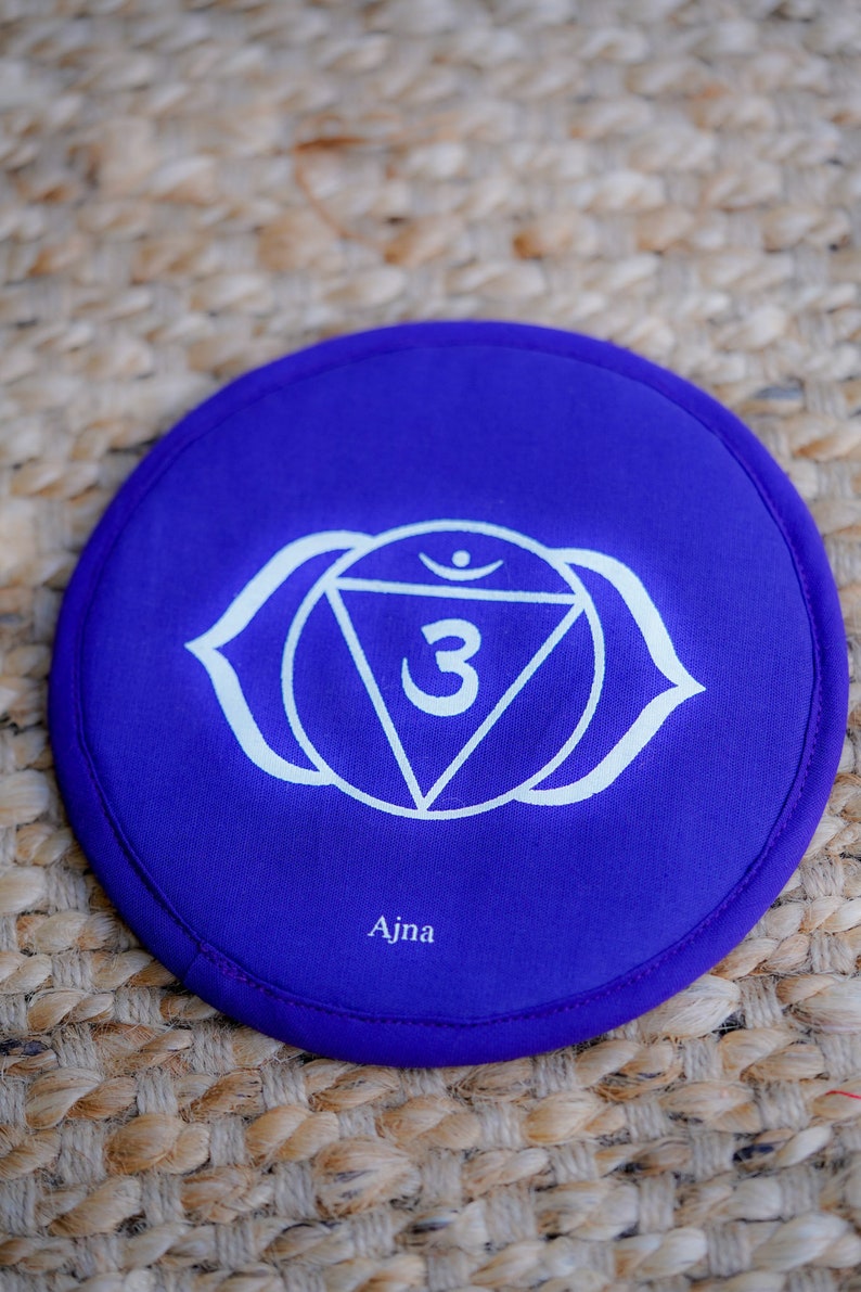 Op de afbeelding: Rond paars kussen met een wit symbool van de derde oog chakra, Ajna, met het nummer 3 in een driehoek.