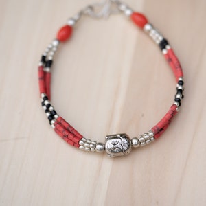 May include: A red and black beaded bracelet with a silver Buddha charm.