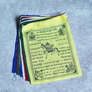 May include: A set of colorful prayer flags with Tibetan text and images. The flags are yellow, green, blue, red, and white. The text on the flags is in Tibetan script and includes a prayer for peace and happiness. The flags are often hung outside of homes and businesses in Tibet and other parts of the Himalayas.