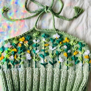 May include: A green knitted halter top with embroidered flowers in shades of white, yellow, and green.