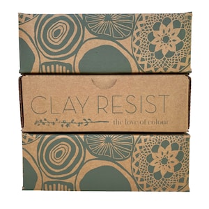 Könnte beinhalten: Drei gestapelte Kartons mit einem grün-braunen Muster. Der mittlere Karton trägt den Text "CLAY RESIST the love of colour".