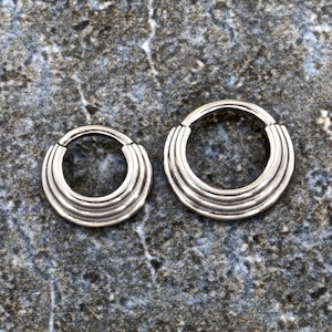May include: Two silver seamless hoop earrings with a ridged design. The earrings are different sizes.