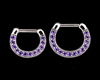 Puede incluir: Dos anillos de septum plateados con una fila de piedras preciosas púrpuras alrededor del borde exterior.