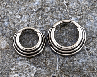 May include: Two silver seamless hoop earrings with a triple-layered design. The hoops are different sizes.