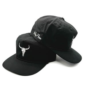 May include: Two black baseball caps with a white skull and horns design on one cap and the text "Molly Proos" on the other.