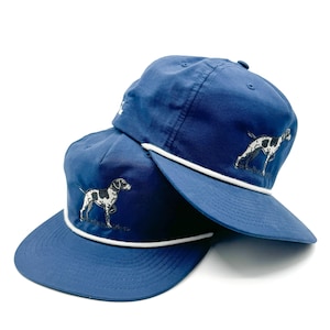 May include: Two blue baseball caps with white rope trim and an embroidered image of a black and white dog.