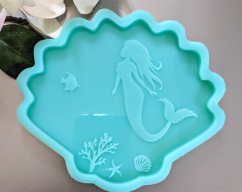 May include: A teal blue silicone mold shaped like a seashell with a mermaid, starfish, seashell, and coral design.