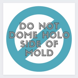 May include: A white square graphic with a teal blue circle and a diagonal line through it. The text within the circle reads "DO NOT DOME HOLO SIDE OF MOLD" in a gray, outlined font.