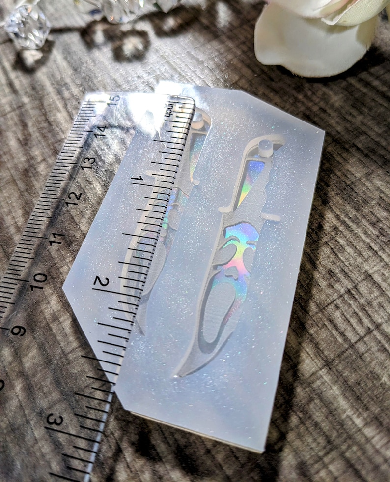 May include: A clear silicone mold with a knife design, approximately 5 inches long. The knife has a decorative handle and a holographic effect. A ruler is placed next to the mold for measurement. The mold is on a wooden surface.