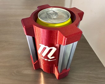 May include: Red and silver can cooler with a white "M" logo. The cooler is holding a yellow can.