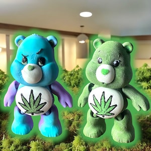 May include: Two plush Care Bear-like figures with a marijuana leaf design on their chests. One figure is blue and the other is green.
