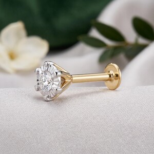 May include: A gold labret stud earring featuring a round, clear, faceted gemstone set in a six-prong silver-toned metal setting. The post is smooth gold-toned metal, ending in a flat, circular gold-toned backing disc for secure placement.