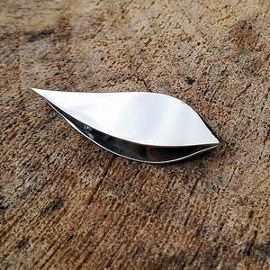 Puede incluir: Un dedal de coser de plata en forma de hoja con una superficie lisa y brillante.
