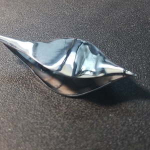 Könnte beinhalten: Eine silberne, metallische, abstrakte Skulptur in Form eines Vogels mit einem langen, spitzen Schnabel.