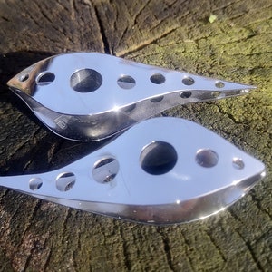 May include: Two silver metal kitchen tools with a teardrop shape and multiple holes. The tools are on a wooden surface.