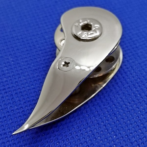 Op de afbeelding: Een zilverkleurige metalen bootklem met een afgerond, puntig uiteinde en een kleine schroef aan de zijkant. De klem heeft een klein, rond gat in het midden.