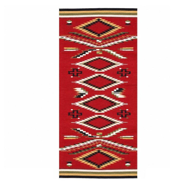 May include: A rectangular woven rug featuring a vibrant red background with a repeating geometric pattern of diamonds and crosses in black, white, and tan. The top and bottom edges are finished with horizontal stripes in black, white, and olive green.