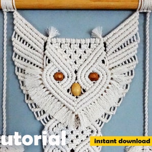 Peut inclure: Une suspension murale en macram&eacute; en forme de hibou blanc avec des yeux en perles de bois. Le hibou est suspendu &agrave; une baguette en bois. Le texte "Tutoriel" et "t&eacute;l&eacute;chargement instantan&eacute; pdf" est en bas de l'image.